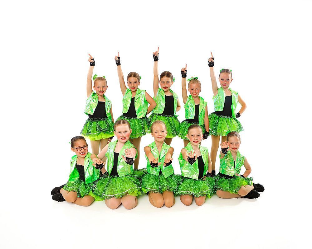 Group of young dancers in bright green costumes posing in two rows on a white background