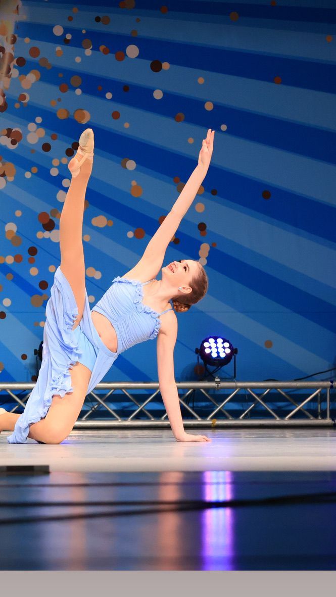 Contemporary dancer balancing on one hand, leg raised, on a blue-lit stage