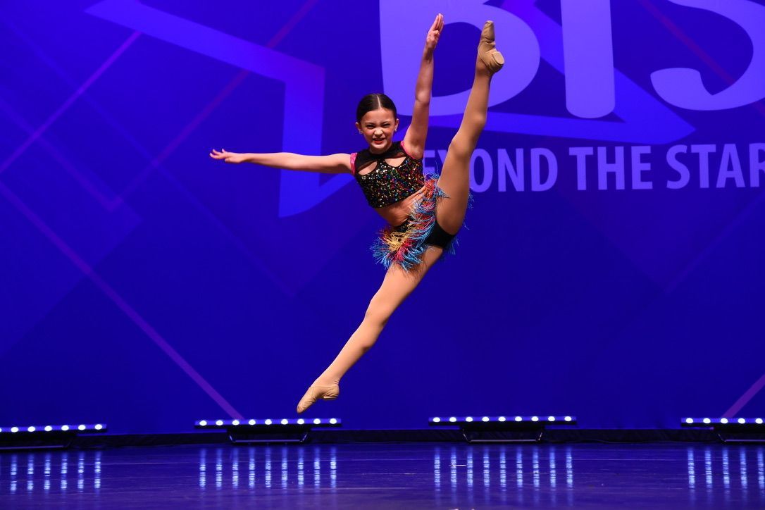Dancer performing a high leg extension on a purple-lit stage with “Beyond the Stars” backdrop