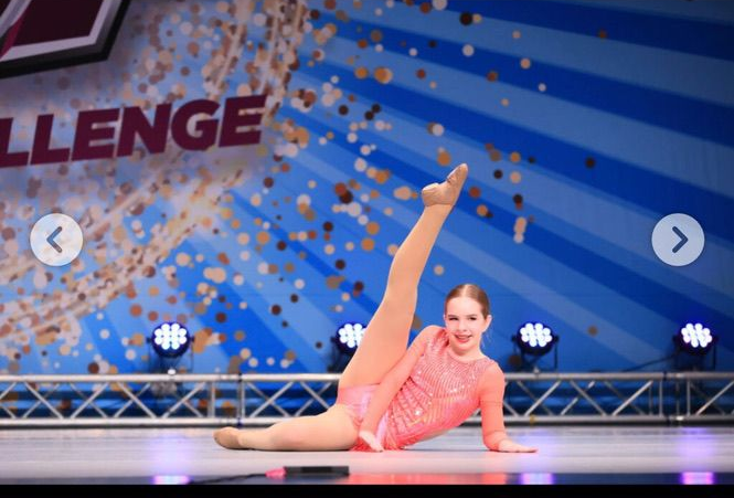 Contortionist in pink leotard posing on stage with one leg raised against a blue backdrop