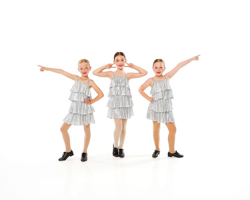 Three children in silver fringe costumes posing on a white background, pointing and saluting.