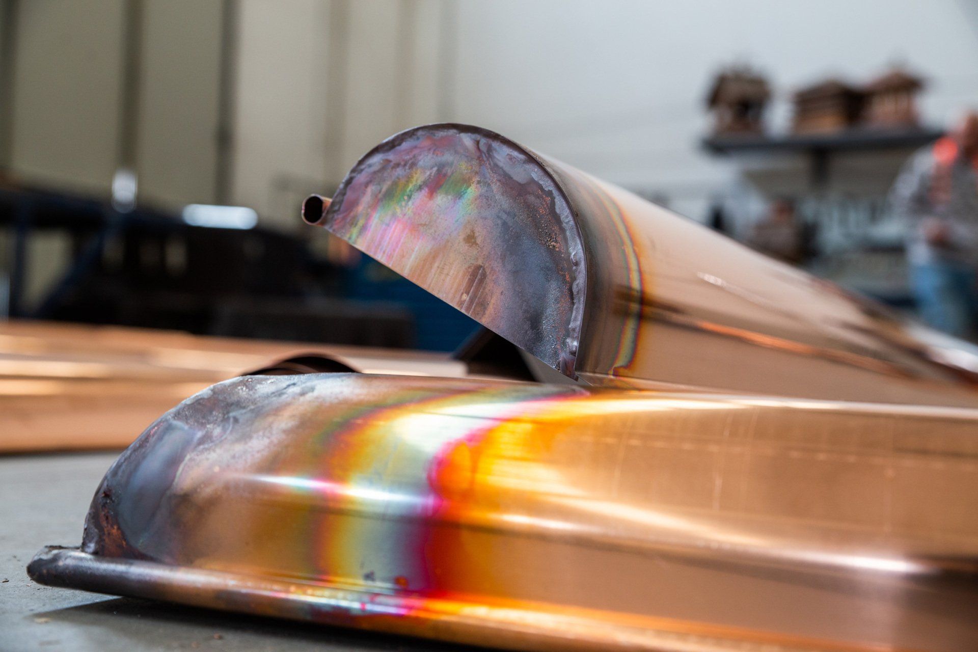 Primo piano di una saldatura su tubi metallici, che mostra la decolorazione dovuta al calore con effetto arcobaleno e lo sfondo di un'officina.