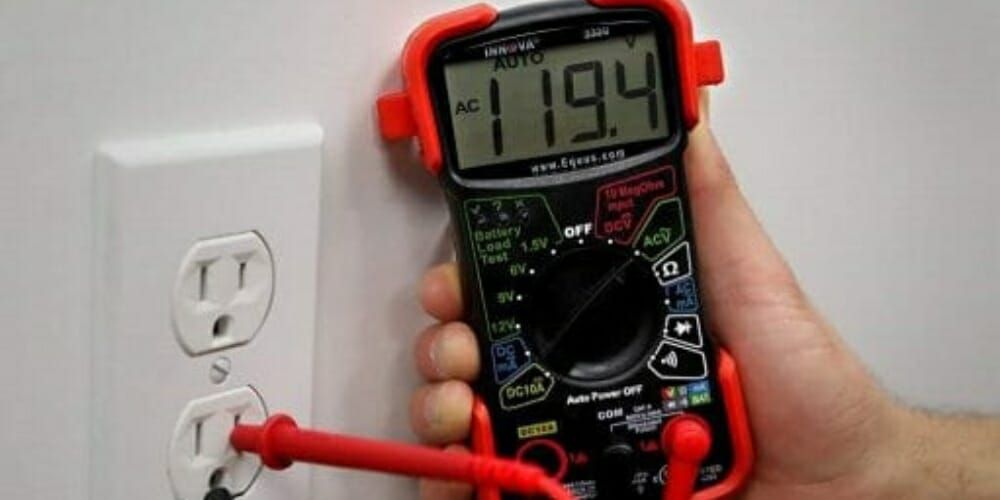 A person is using a digital multimeter to test an outlet.