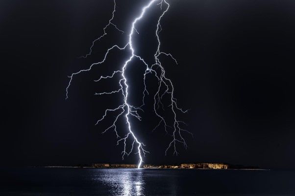Lightning strikes over a body of water at night