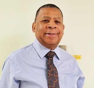 A man in a blue shirt and tie is smiling for the camera.