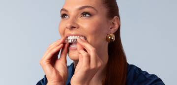 A woman is putting a clear brace on her teeth.