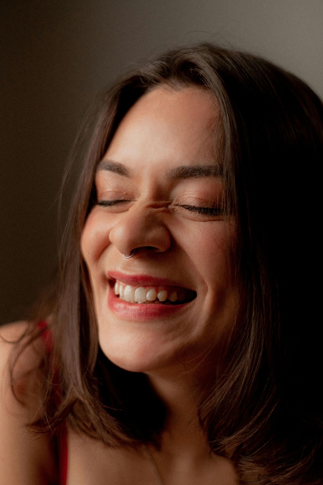 A woman with a nose ring is smiling with her eyes closed.