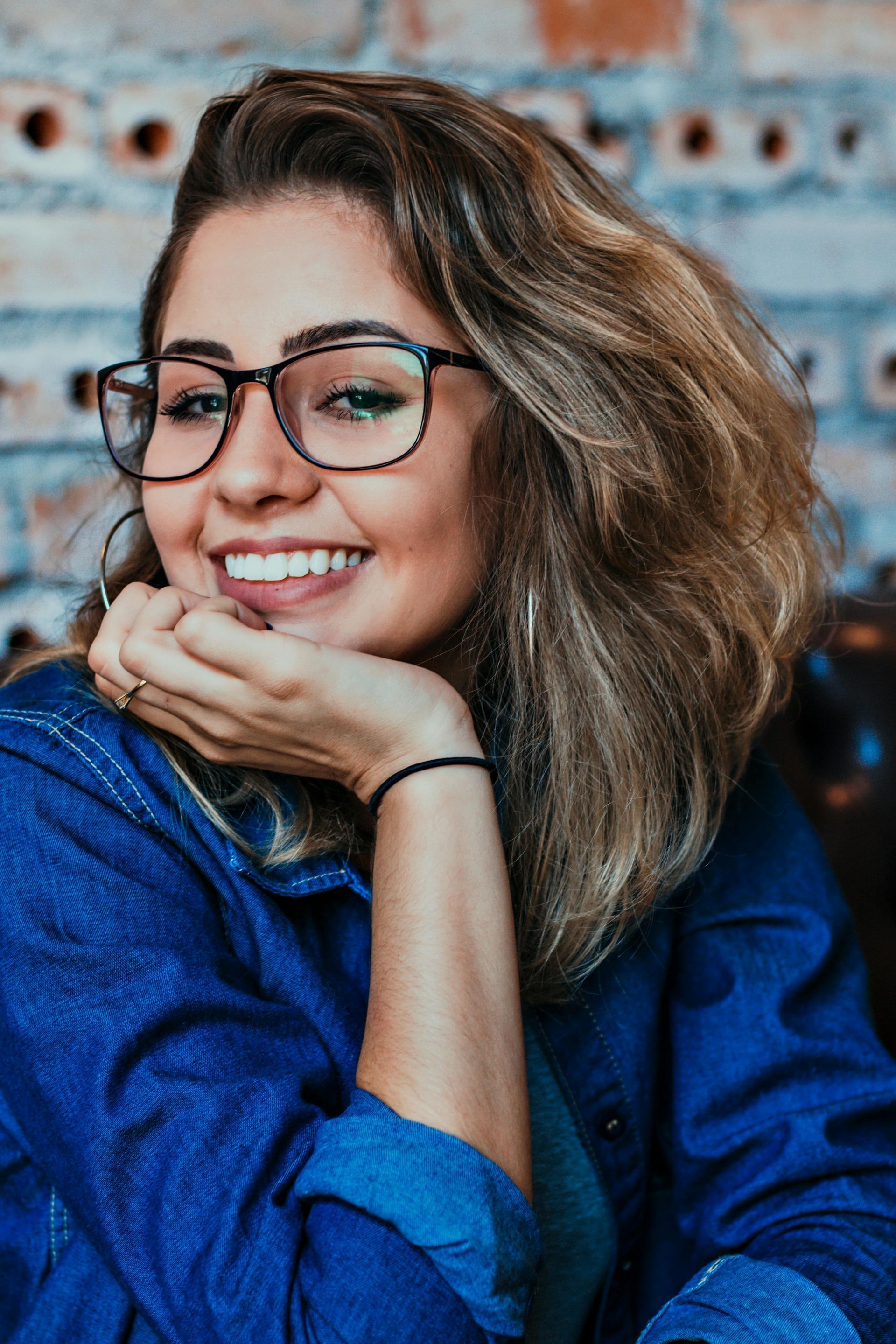 A woman wearing glasses and a blue shirt is smiling.