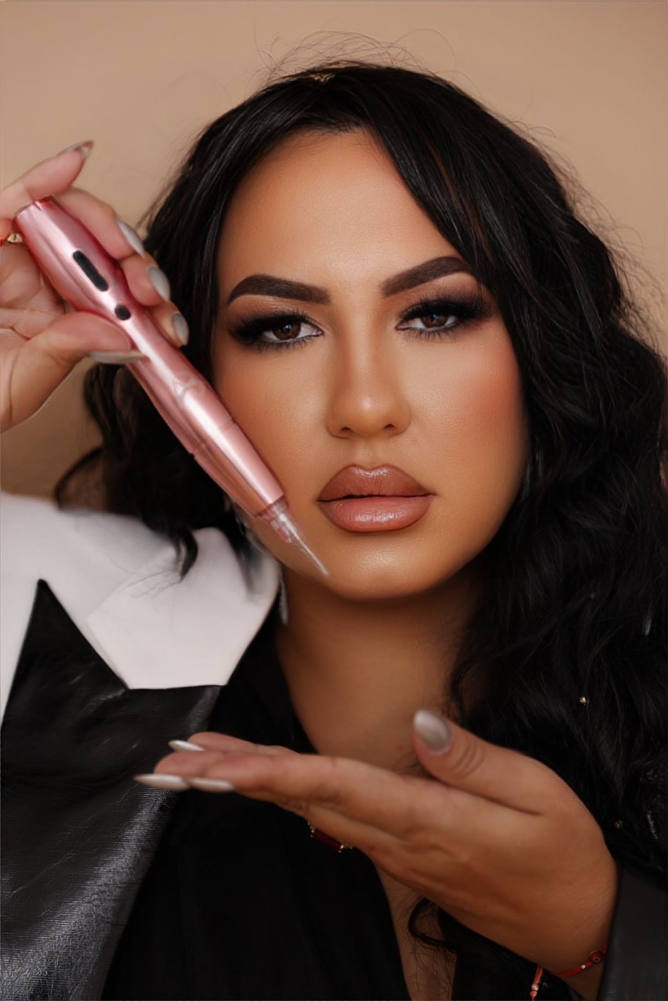 Woman holding a pink cosmetic pen, in front of a neutral backdrop. She has dark hair and a serious expression.