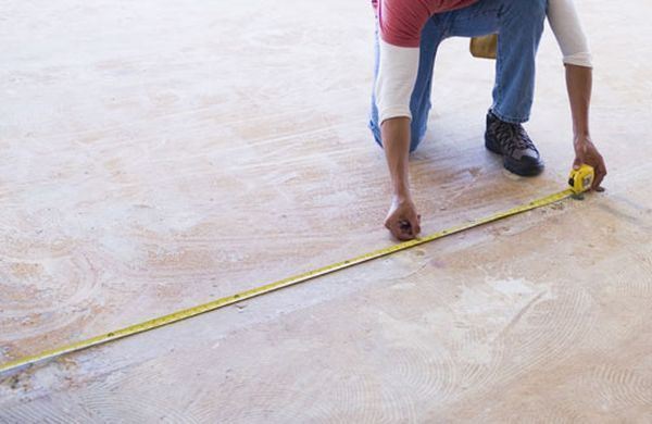 Person crouching to measure a floor with a yellow tape measure