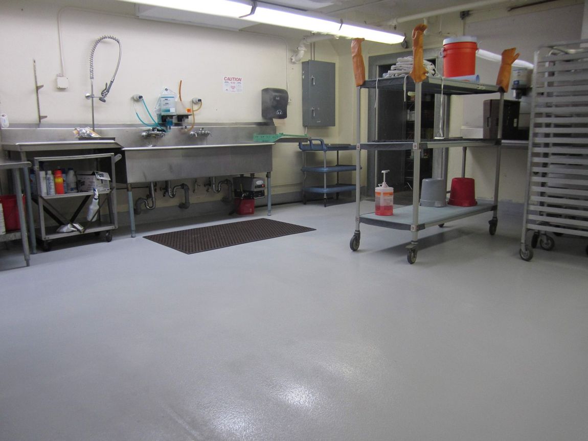 A clean industrial kitchen with stainless steel counters, shelving, and a polished gray floor.