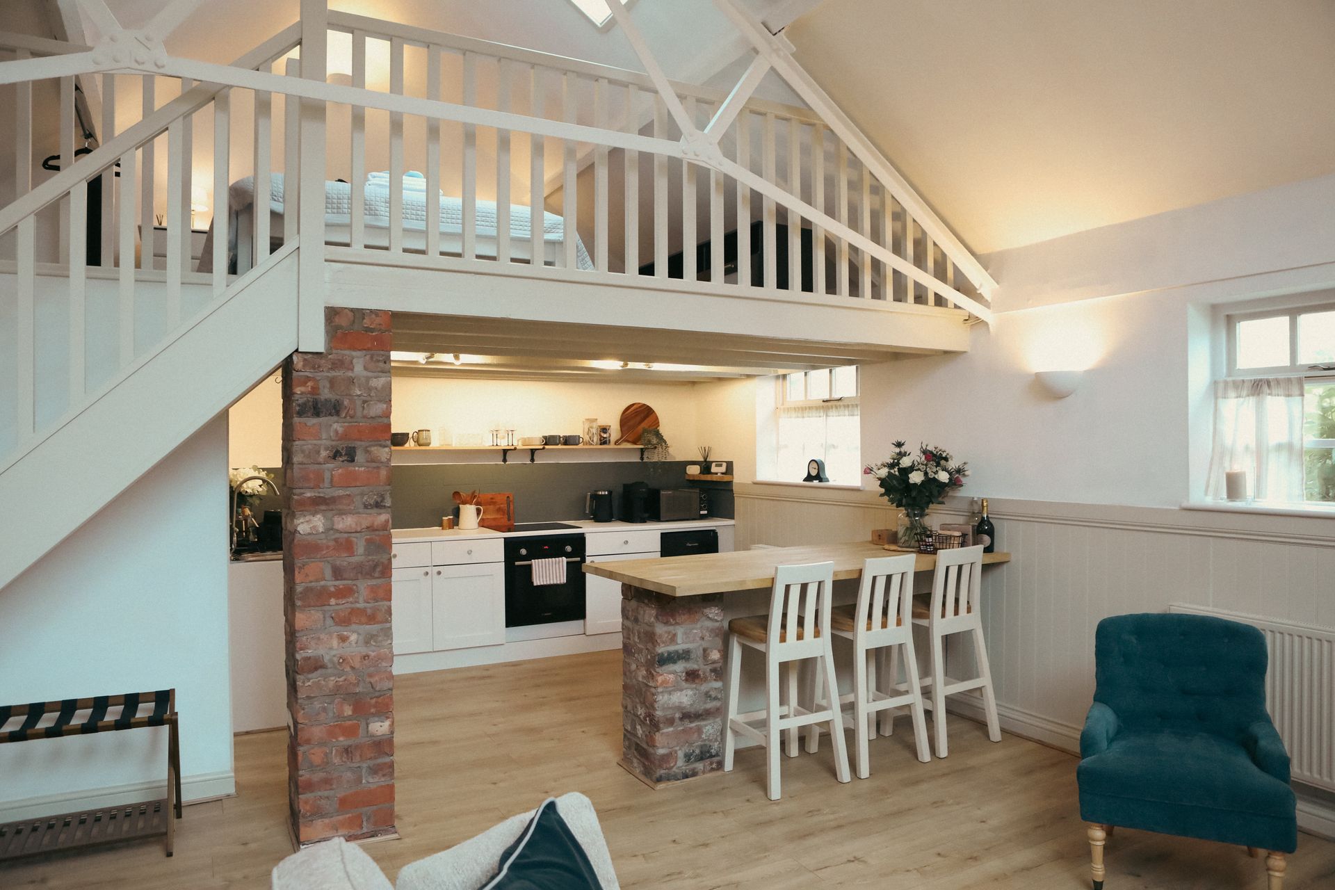 Open loft kitchen and living room with white railings, brick accents, and teal chair