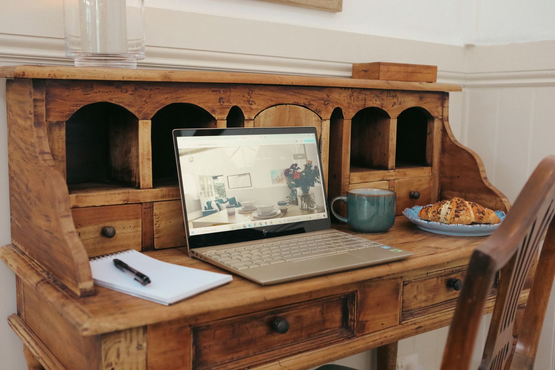 Laptop on a wooden desk with notebooks, a mug, and a plate of cookies in a home office corner
