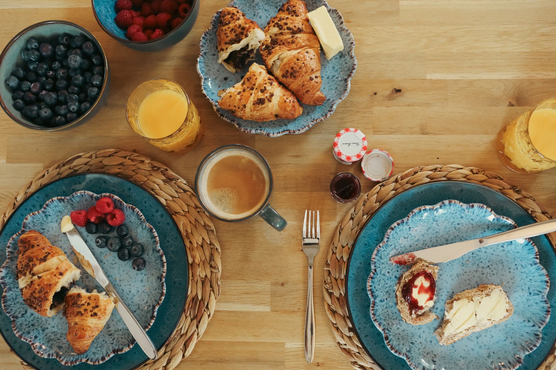 Breakfast spread with pastries, berries, orange juice, and coffee on a wooden table