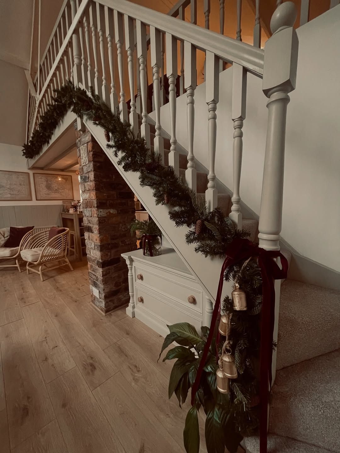 LaplandUK Staircase with white banister decorated in green garland, beside a brick fireplace and white cabinet