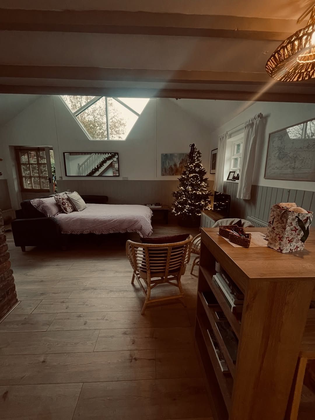 LaplandUK Cozy attic bedroom with a bed, wicker chair, wooden dresser, and a lit Christmas tree.