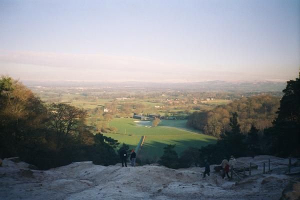 Panoramic view from a hilltop over a green valley at sunset, with a few people on the rocky foreground