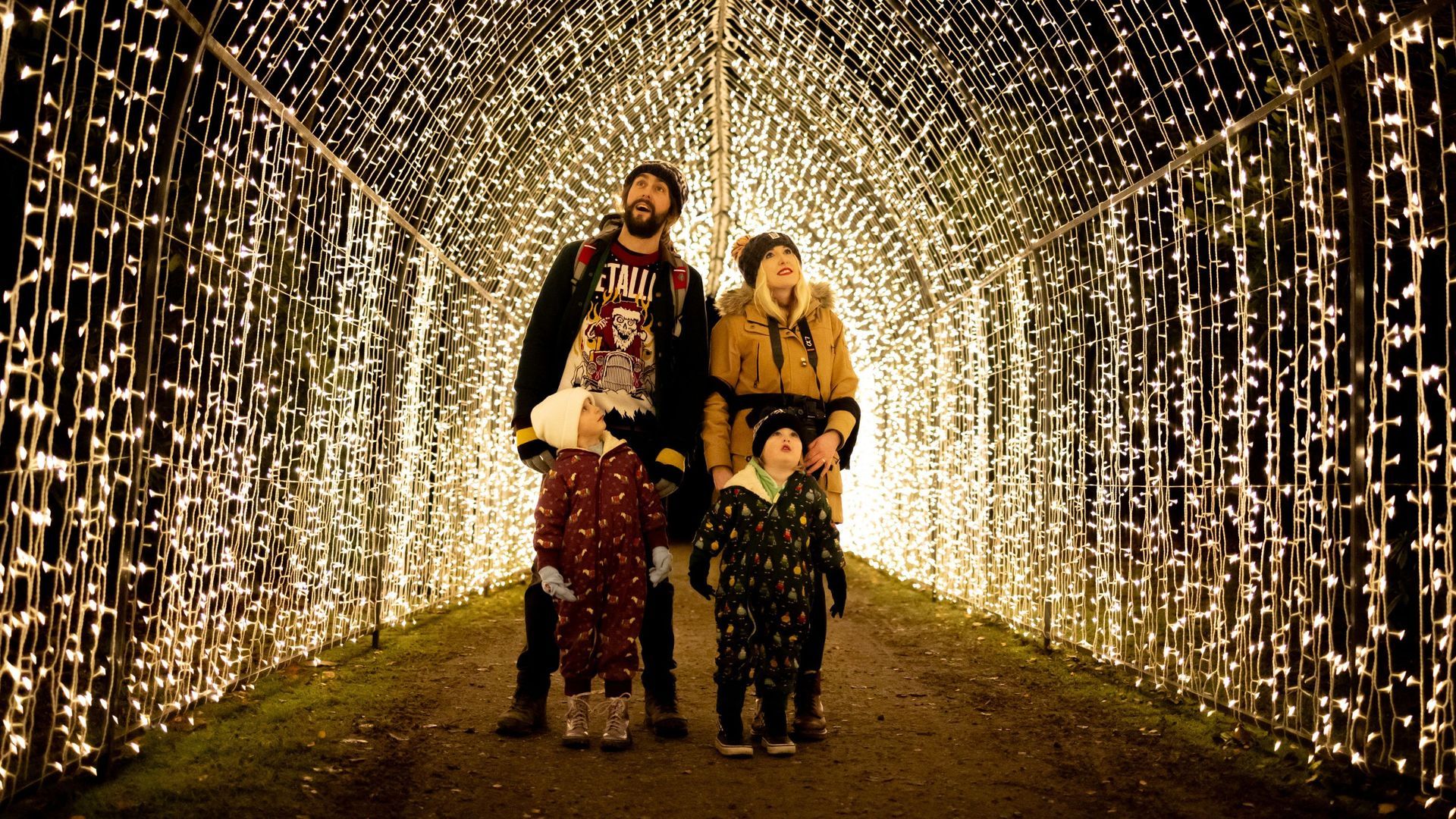 LaplandUK Two people walking through a tunnel of warm white string lights at night