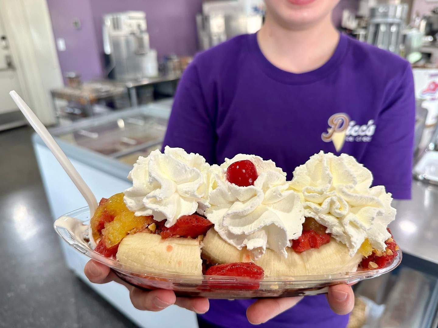 Person holding a platter topped with whipped cream and fruit in a kitchen.
