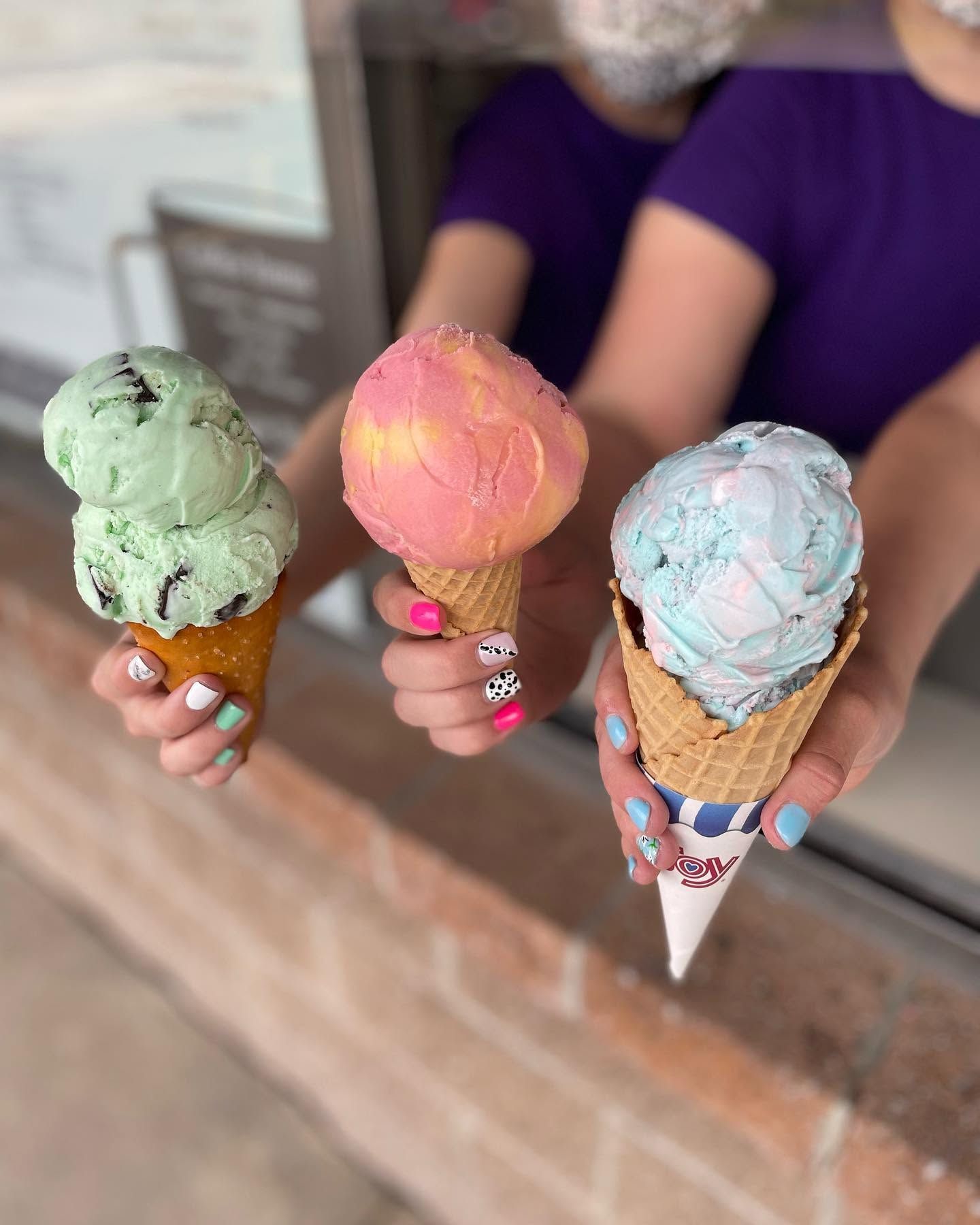 Three hands holding various ice cream cones at a shop counter