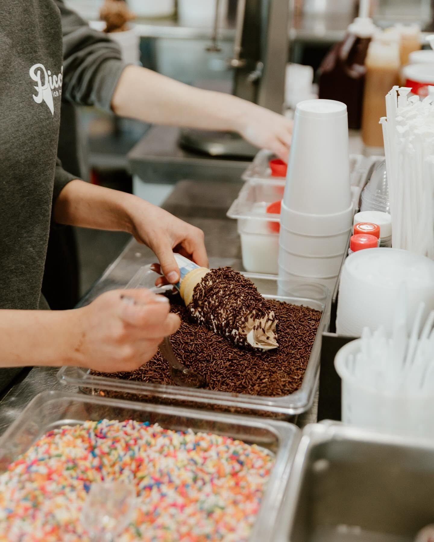 Hands scooping chocolate ice cream with sprinkles at a dessert counter