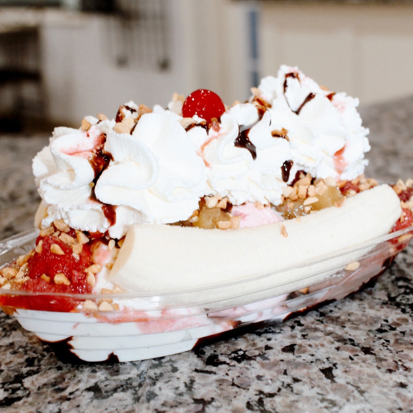 Banana split sundae topped with whipped cream, fruit, and syrup in a glass dish