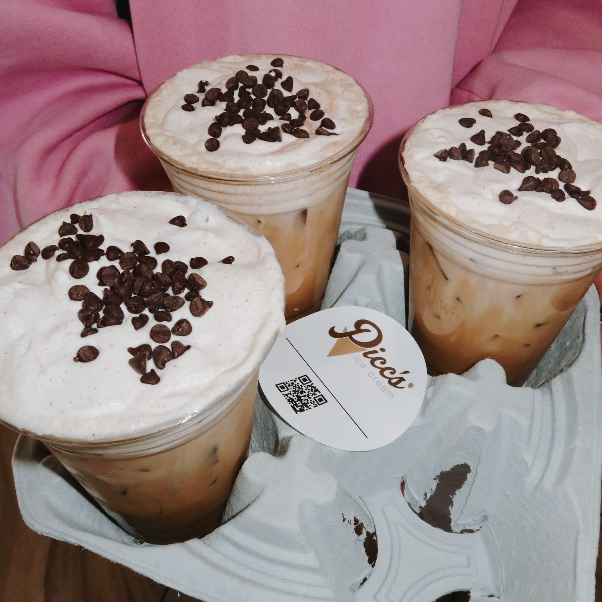 Three iced coffee drinks topped with whipped cream and chocolate chips on a tray