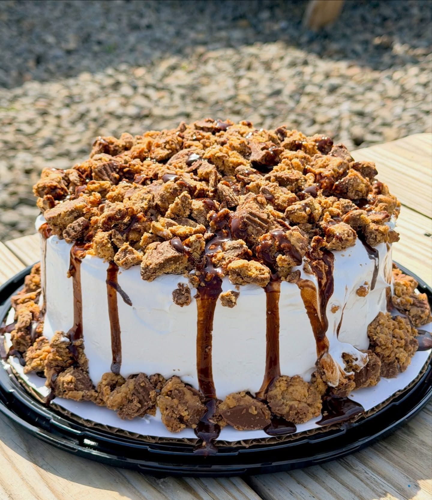 White frosted cake topped with caramel-drizzled crumble on a black tray outdoors