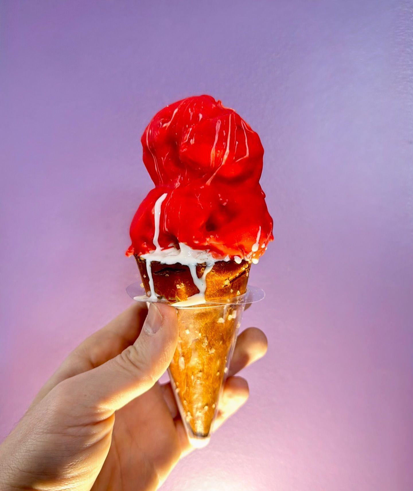 Hand holding a cone topped with bright red ice cream against a purple background