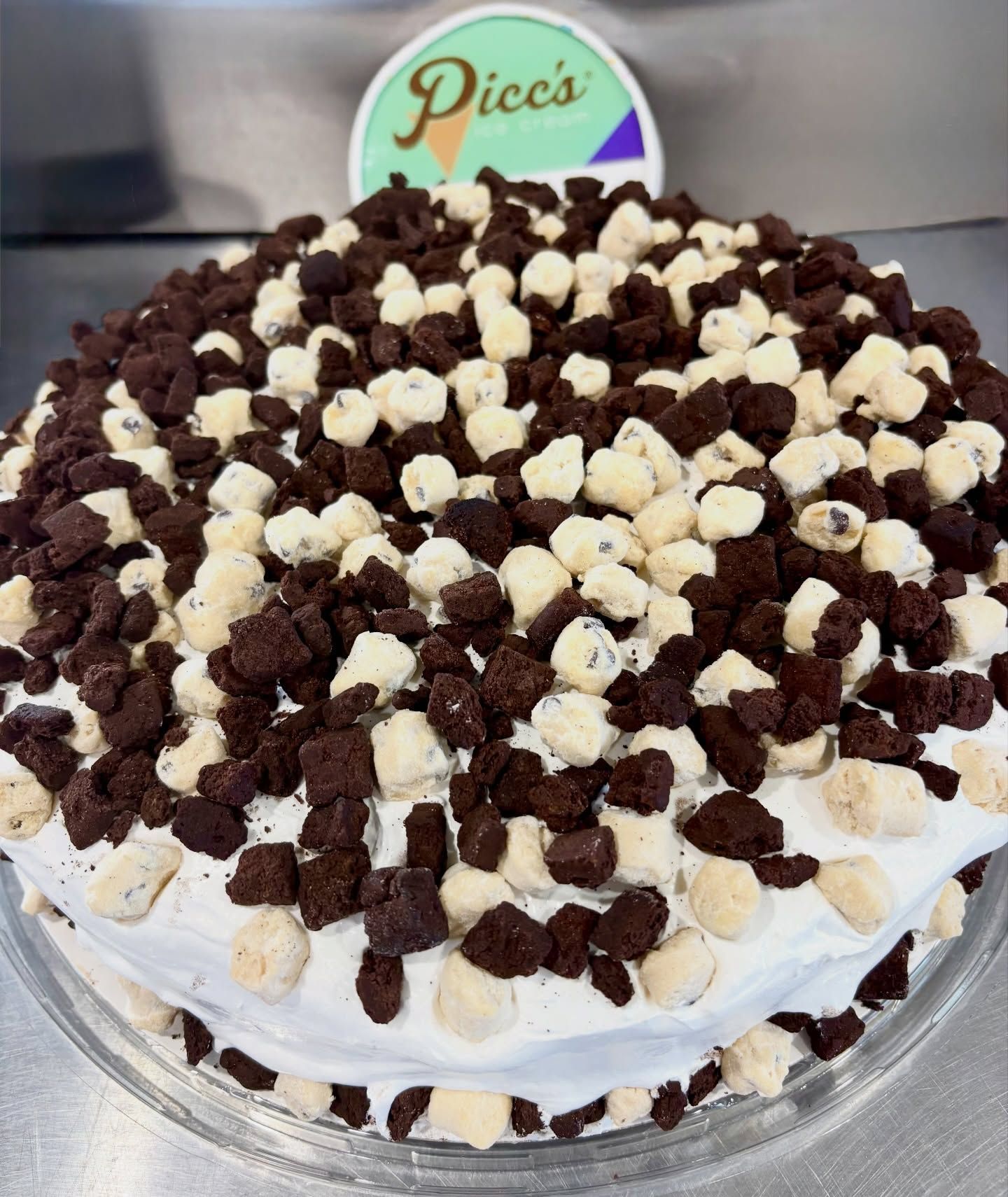 Chocolate cookie crumble cake with white frosting and cream topping on a clear stand
