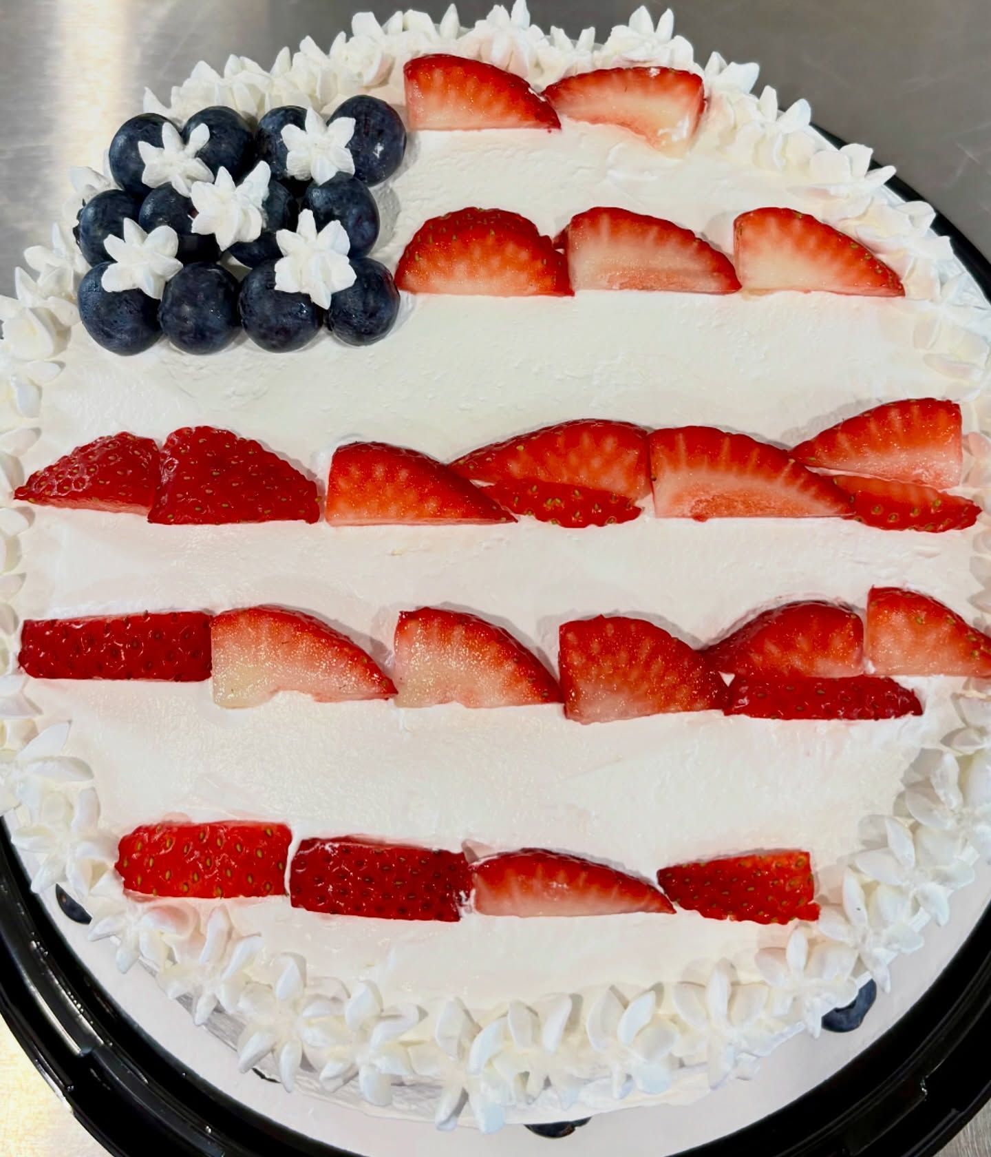 Round white-frosted cake topped with strawberries and blueberries in a red, white, and blue striped pattern