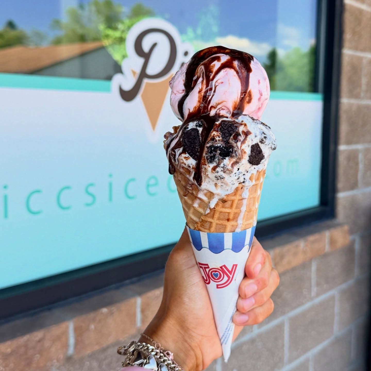 Hand holding a waffle cone with chocolate-drizzled ice cream outside a shop window