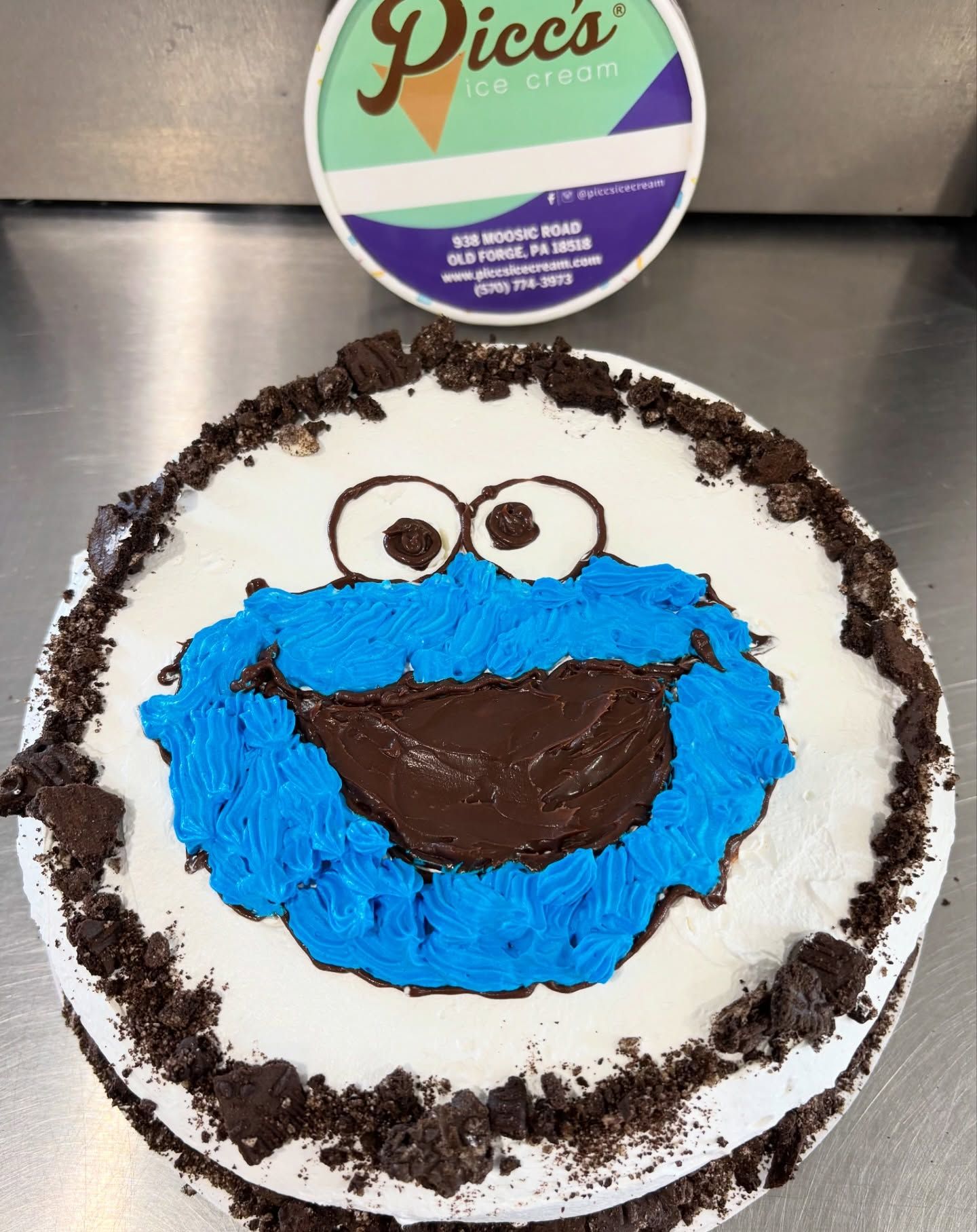 Cookie cake decorated like Cookie Monster with blue frosting, big eyes, and a smiling mouth