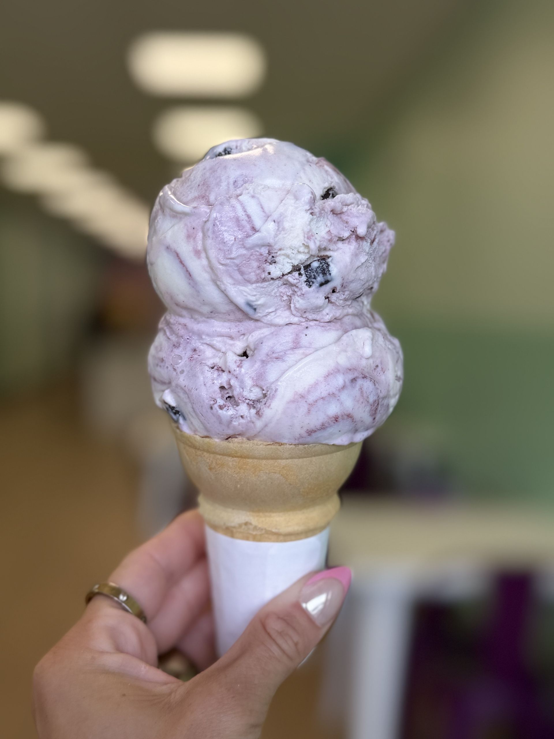 Hand holding a double raspberry truffle ice cream cone in a white cup