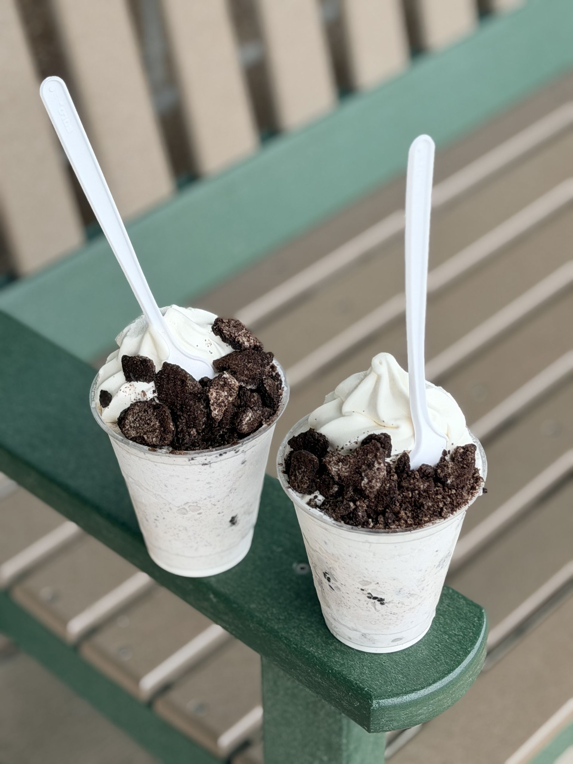 Two small cups of Oreo Flurry dessert with spoons on a green bench outdoors