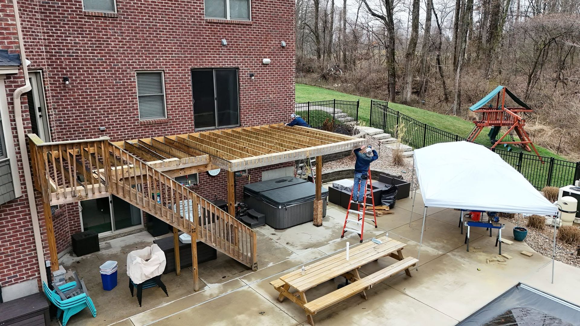 Backyard deck under construction beside brick house, with ladder, tools, and workers