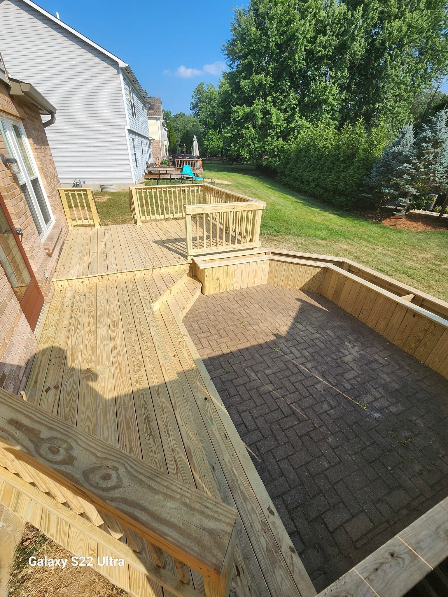 Wooden backyard deck with steps, railing, and a person in blue near a house and green lawn.
