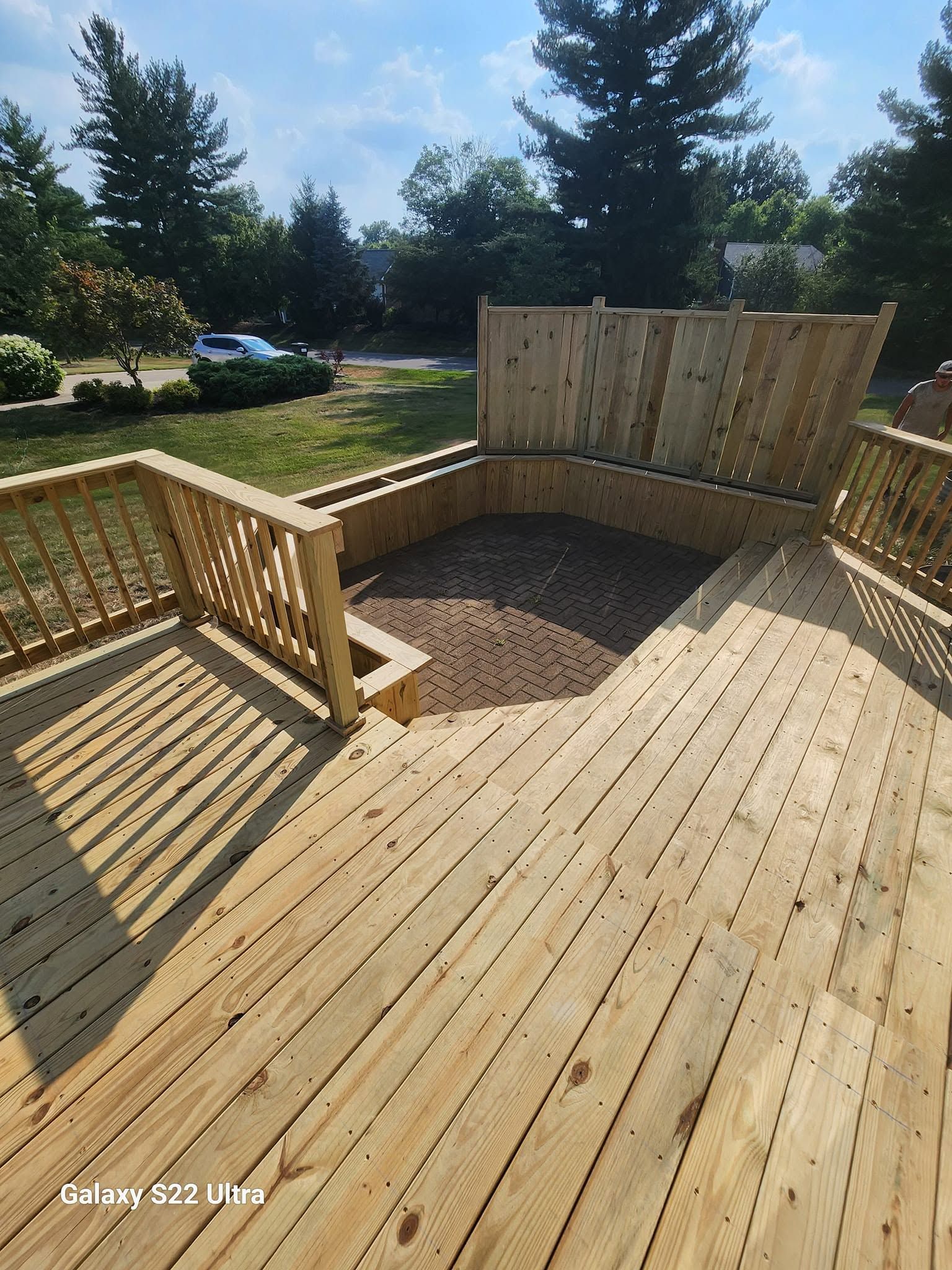 Wooden backyard deck with built-in benches and railing, overlooking a yard with trees and gravel area.