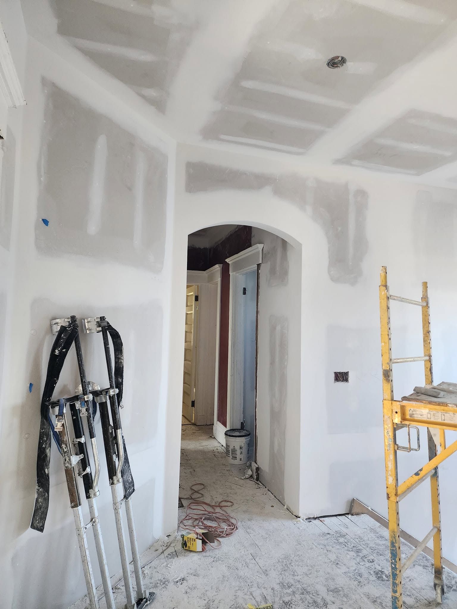Unfinished drywall room with doorway, scaffolding, and tools during renovation.