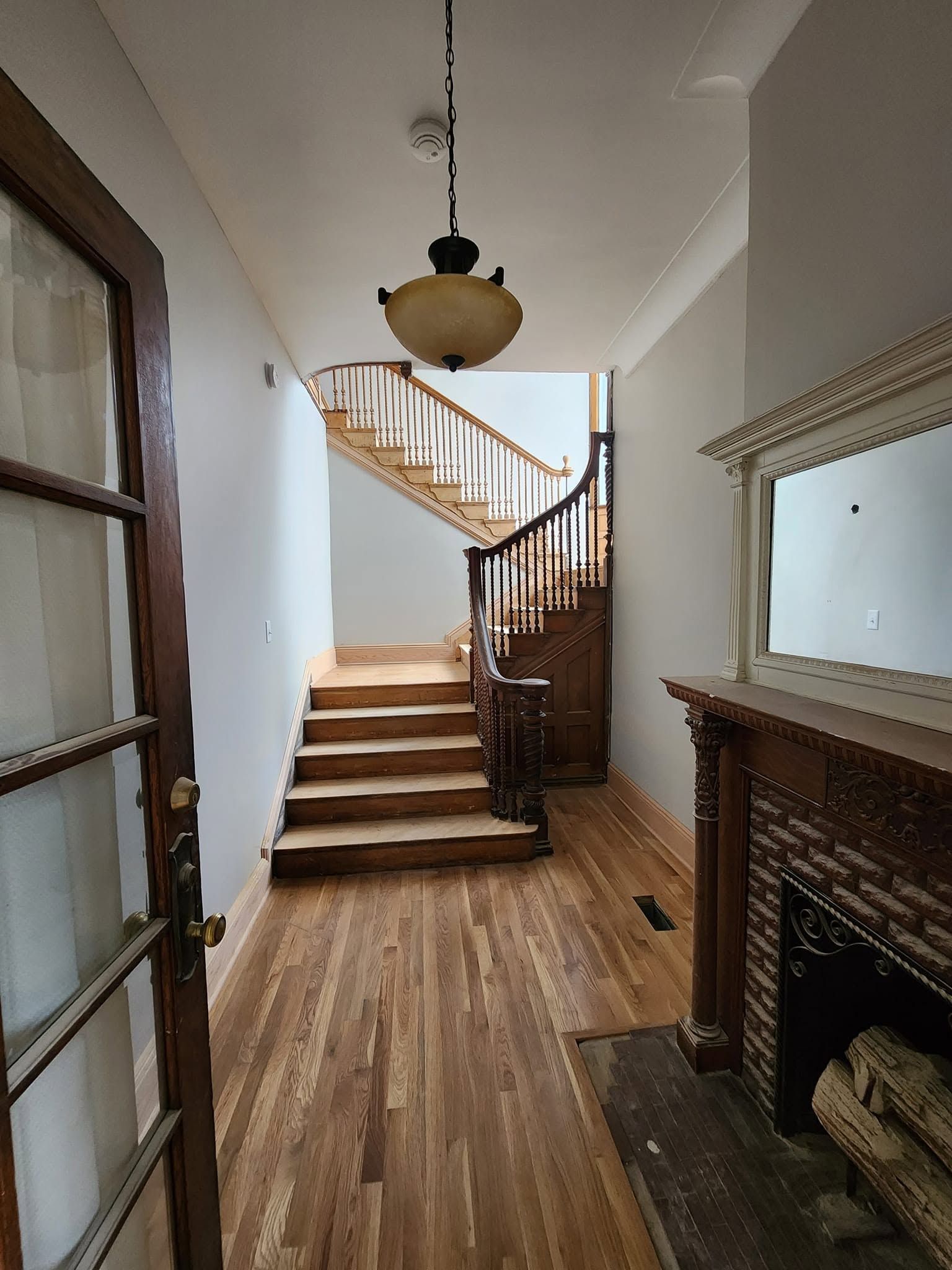 Narrow hallway with wooden stairs, white walls, hardwood floors, and a fireplace on the right.