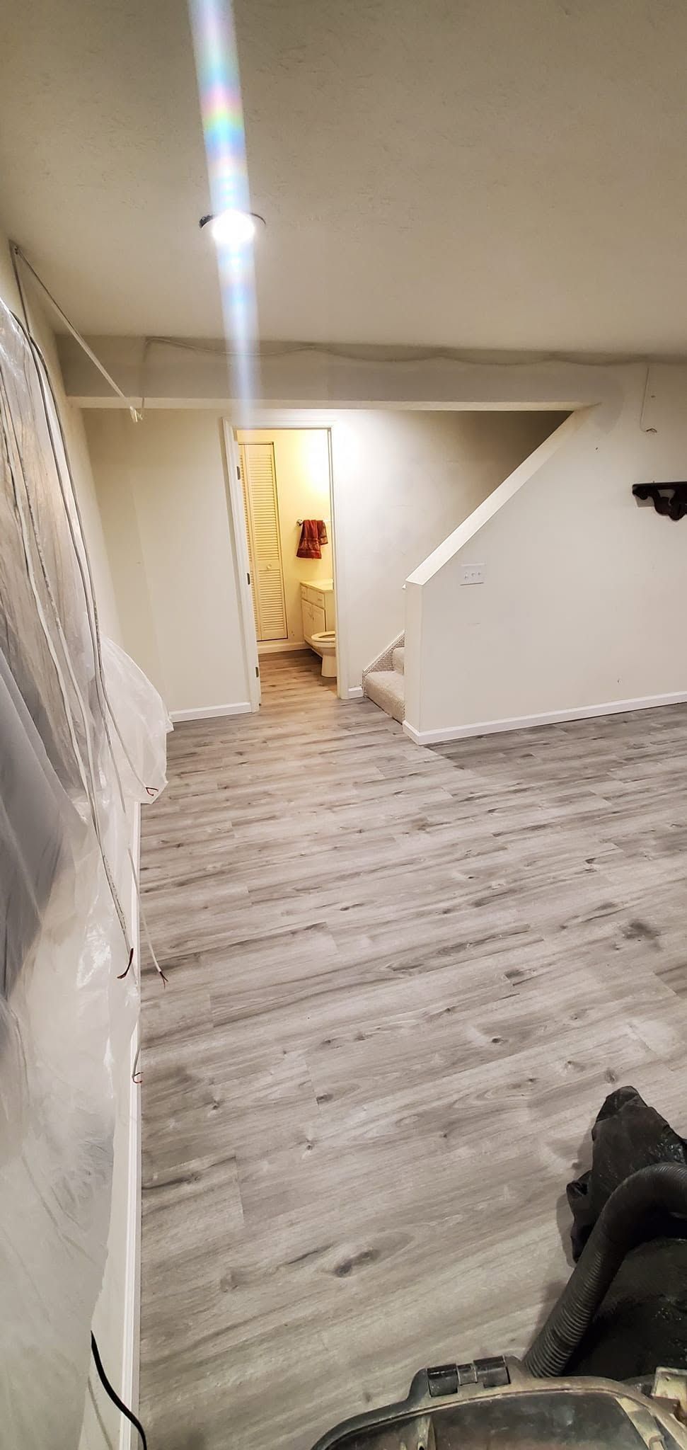 Hallway with light wood floor, white walls, stair railing, and an open doorway at the end