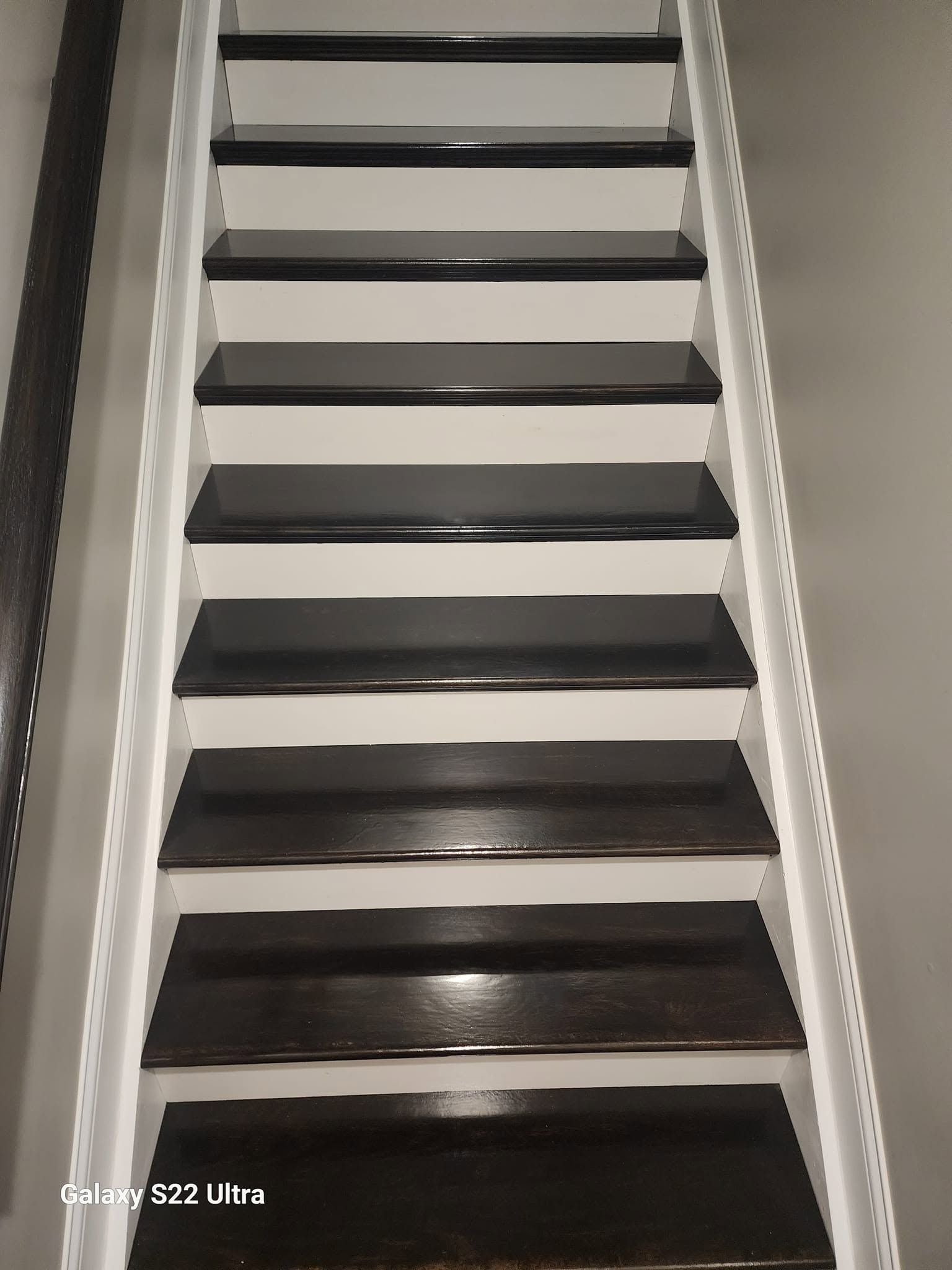 Steep staircase with dark steps and white side rails, viewed from below.
