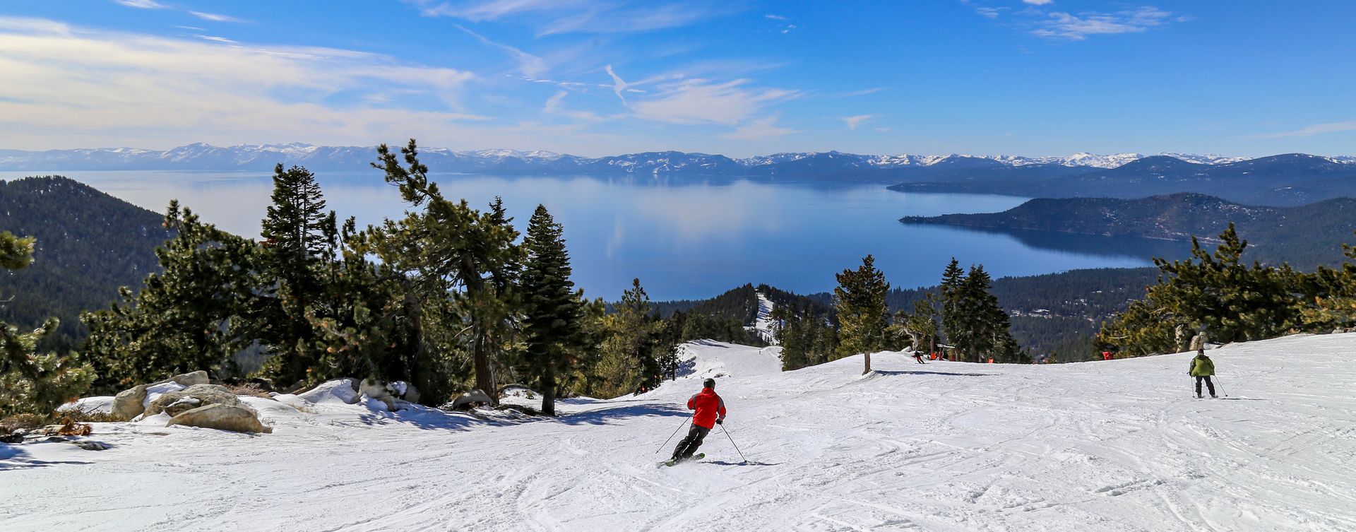 A group of people are skiing down a snow covered slope with a lake in the background.