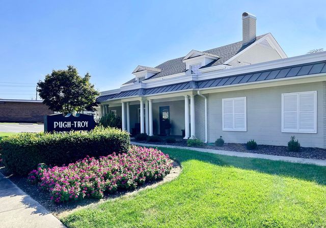 Bright suburban house with a manicured lawn, pink flower bed, and a sign by the entrance