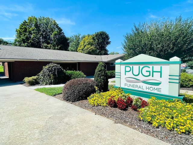 Pugh Funeral Home sign beside a brick building, driveway, and landscaped flowers on a sunny day