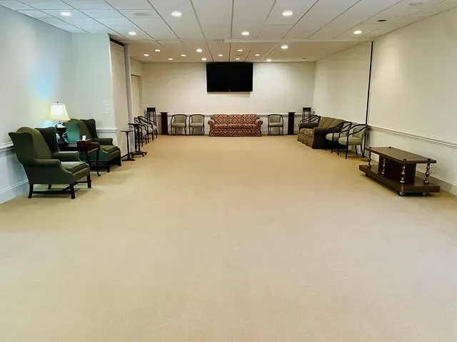 Empty beige multipurpose room with chairs, couches, and a wall-mounted TV.
