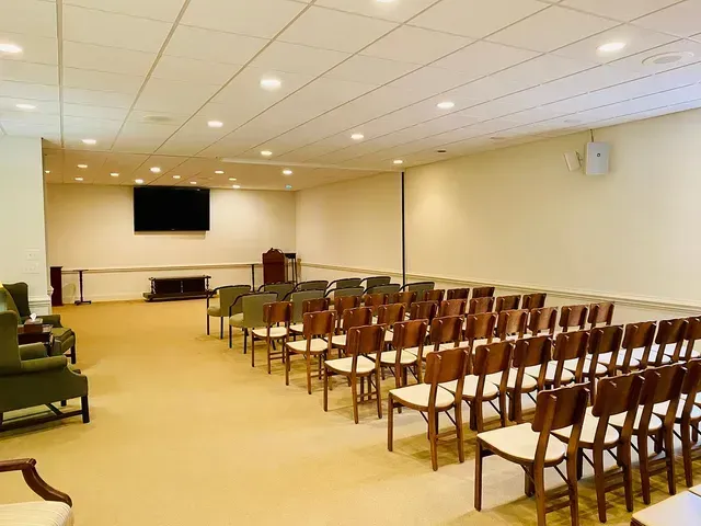 Empty conference room with rows of wooden chairs facing a screen and podium