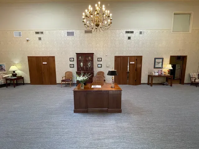 Large hall interior with a central desk, chandelier, wooden doors, and chairs along the walls.