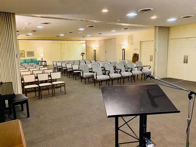 Empty meeting room with rows of chairs and a podium on a carpeted floor, lit by recessed ceiling lights