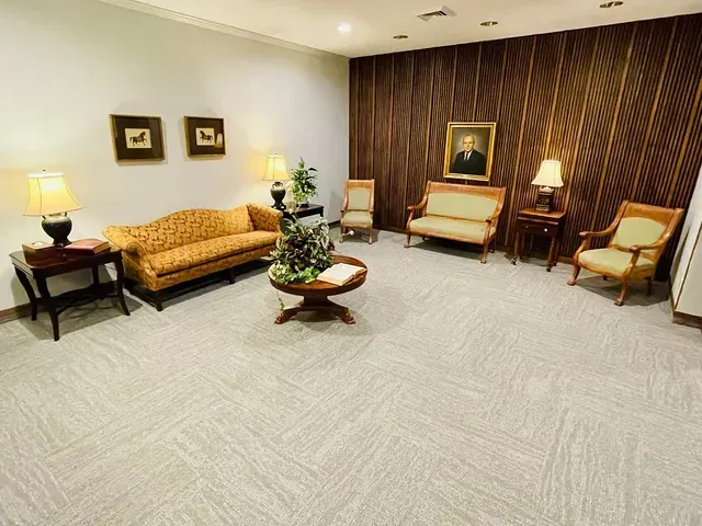 Spacious hotel lobby with beige sofas, chairs, lamps, and a wood accent wall with framed art